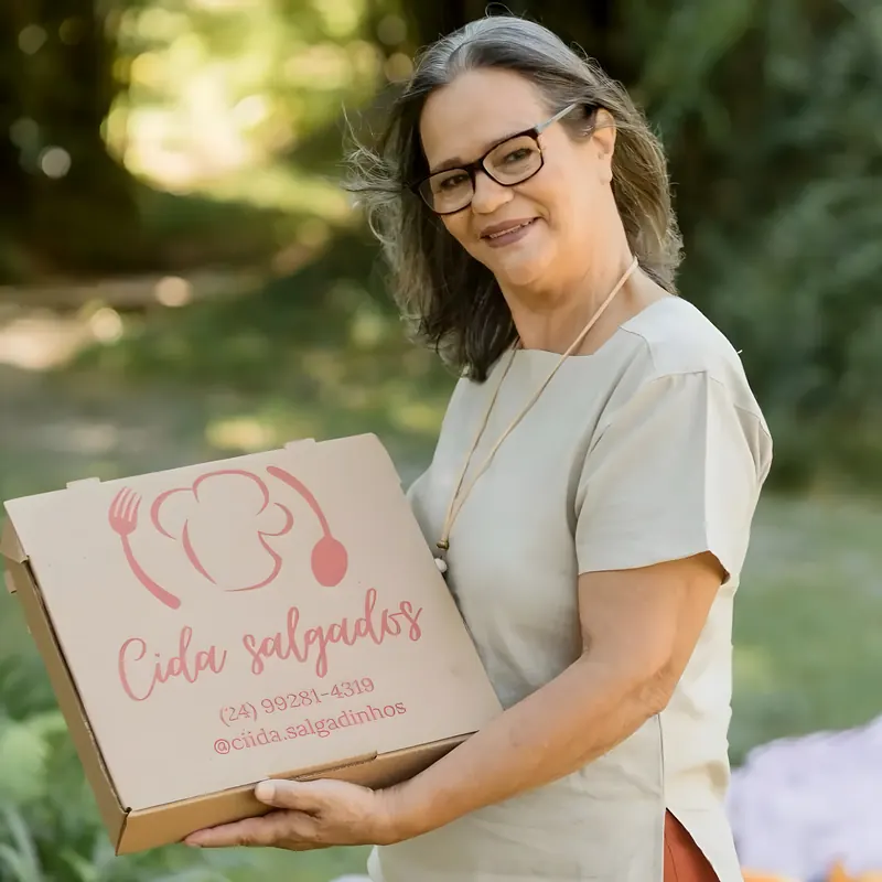 Dona Cida segurando a caixa artesanal de salgadinhos